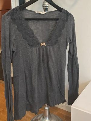 3 långärmade loungewear-toppar - Säljer 3 ribbade långärmade toppar i loungewear-stil, en i mörkgrått och en i vitt. Båda har spetsdetaljer runt den djupa v-ringningen och en liten rosett framtill. Perfekta för mysiga hemmakvällar. Materialet känns mjukt och stretchigt. Jättebra sick förutom en fläck på den rosa