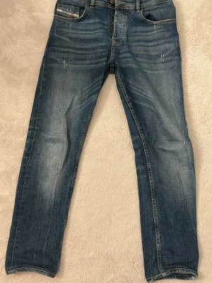 Blå raka jeans från G-Star RAW - Säljer ett par blå jeans från G-Star RAW med raka ben och klassisk femficksmodell. Jeansen har slitningar och ljusa tvättade partier för en cool, avslappnad look. Stängs med knappar och har detaljerade sömmar. Perfekta till vardagsstilen.