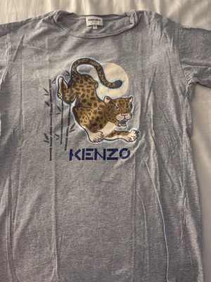 Grå Kenzo t-shirt med leopardtryck - Snygg grå t-shirt från Kenzo med ett stort leopardtryck och bambumotiv på bröstet. T-shirten har korta ärmar, rund halsringning och är gjord i mjuk bomull. Perfekt för dig som vill sticka ut med ett coolt djurmönster och streetwear-vibe.