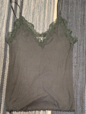 Grön ribbad linnetopp från Amisu - Snygg grön ribbad linnetopp från Amisu med spetsdetaljer längs v-ringningen och tunna axelband. Perfekt att styla lager på lager eller bära som den är. Materialet känns mjukt och följsamt.