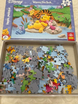 Winnie the Pooh pussel 160 bitar - Disney pussel med motiv av Nalle Puh, Tiger och Nasse som vilar vid en sjö. Pusslet har 160 bitar och färgglada illustrationer. Lådan är blå och visar karaktärerna på framsidan. Passar från 5 år och uppåt.
