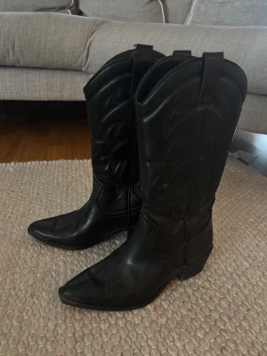 Svarta cowboy boots i läder - Snygga svarta cowboy boots med klassisk spetsig tå och dekorativa sömmar längs skaftet. Strlk 37