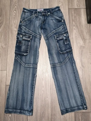 Low Waist jeans  - Säljer nu dessa coola cargojeans då de tyvärr var för små för mig. Fint skick! Låg  och rak modell. Står storlek L i men är mer som en XS-S. Stretchiga. Höftmått: 36 cm rakt över (tänk på att dessa jeans sitter under naveln). Innerbenslängd: 79 cm. 