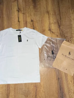 Vit t-shirt från Polo Ralph Lauren - Klassisk vit t-shirt från Polo Ralph Lauren med den ikoniska broderade loggan på bröstet. T-shirten har rund hals och korta ärmar. Tillverkad i mjuk bomull för en skön och stilren look. Perfekt basplagg till garderoben. Priset går att diskutera vid snabb affär