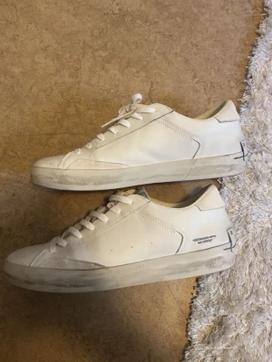 Vita sneakers från Crime London - Snygga vita låga sneakers från Crime London i läder med klassisk design och vita snören. Diskret textdetalj på sidan och bak på hälen. Perfekta för en clean och stilren look.