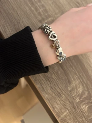Pandora silverarmband med berlocker - Säljer ett snyggt Pandora armband i silver med flera unika berlocker, bland annat hjärtan, stjärna och en ros. Armbandet har detaljer i både silver och guldton och är perfekt för dig som gillar personliga smycken. Passar till alla tillfällen och är lätt att matcha med andra accessoarer.