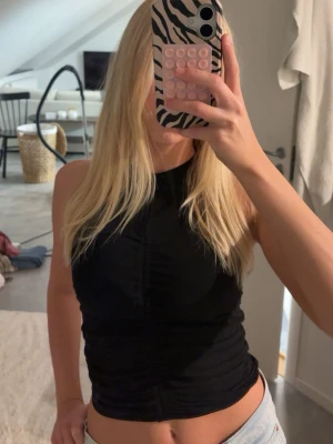 Svart ärmlös croppad topp - Snygg svart ärmlös topp med croppad passform och rund hals. Perfekt till jeans eller kjol för en trendig look. Materialet känns mjukt och stretchigt, vilket gör den bekväm att bära hela dagen.