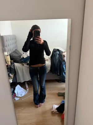 Mörkblå bootcut jeans med låg midja - Säljer ett par mörkblå bootcut jeans med låg midja och lätt slitningar på låren. Jeansen har klassisk femficksdesign och stängs med dragkedja och knapp. Perfekta för en avslappnad och trendig look. STORLEK 26/32!!