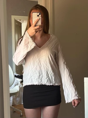 Ljusrosa blus med spetsdetaljer - Söt vit blus med v-ringning och spetsdetaljer vid ärmslut, halsringning och nederkant. Blusen har en avslappnad passform och långa ärmar. Tillverkad i ett tunt, lätt tyg. Skrynklig på bilden men det är bara att stryka!
