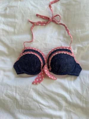 Blå bikiniöverdel med rosa prickiga band💓 - Supersöt bikiniöverdel i mörkblått med jeanslook och rosa detaljer. Band och volangkant är rosa med vita prickar och knyts i nacken. Kuporna är vadderade och har en feminin, lekfull stil. Perfekt för strandhäng eller poolparty!💓