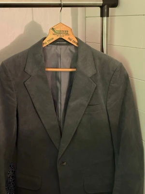 Grå kavaj i mockaimitation - Stilren grå kavaj med klassisk passform och spetsiga slag. Kavajen har två framfickor, en bröstficka och knäppning med en knapp. Materialet ser ut som mockaimitation vilket ger en mjuk och modern känsla. Perfekt för dig som vill ha en snygg och tidlös look. Hör av er vid frågor & funderingar, priset är inte helt hugget i sten!!