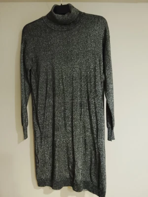 Grå stickad poloklänning NYSKICK - Mysig grå stickad klänning med polokrage och långa ärmar. Perfekt för kyligare dagar och enkel att styla med boots eller sneakers. Klänningen har en rak passform och är knälång. Svart med silver glitter i hela klänningen, snyggt med ett bälte runt midjan. Nyskicka, en gång använd bara. Har likadan i beige som är helt oanvänd.