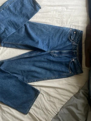 Blå raka jeans i klassisk modell från Weekday  - Säljer ett par blå jeans med rak passform och hög midja. Jeansen har fem fickor, bälteshällor och stängs med dragkedja och knapp. Tillverkade i kraftig denim som ger en tidlös look. Perfekta till en avslappnad stil.