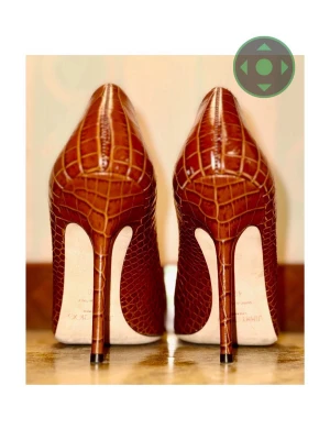 Bruna klackar i krokopräglat läder Jimmy Choo - Snygga bruna klackskor från Jimmy Choo i krokopräglat läder med spetsig tå och hög klack. Skorna har en elegant och tidlös design som verkligen sticker ut. Perfekta för dig som vill ha en lyxig och trendig look.