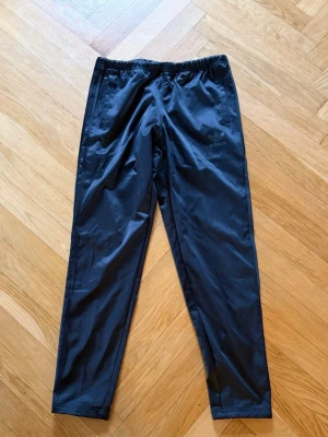 Svarta träningsbyxor från Adidas - Snygga svarta träningsbyxor från Adidas med diskret logga på låret. Byxorna har smal passform, resår i midjan och är tillverkade i ett lätt och följsamt material som passar perfekt för träning eller sport.