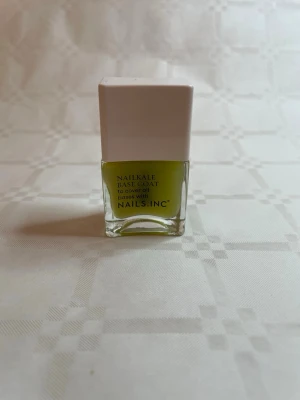 NAILS INC Nailkale Base Coat - NAILS INC Nailkale Base Coat är ett baslack i en fräsch ljusgrön nyans. Kommer i en stilren fyrkantig glasflaska med vit kork. Perfekt för att stärka naglarna och ge en snygg grund inför färgat nagellack.