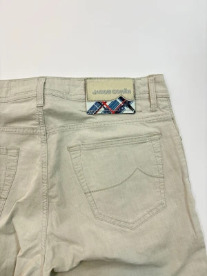 Beige jeans från Jacob Cohën - Snygga beige jeans från Jacob Cohën med klassisk femficksdesign och raka ben. Jeansen har en patch med rutigt mönster och logga bak i midjan. Tillverkade i mjukt bomullstyg för en skön känsla och stilren look.