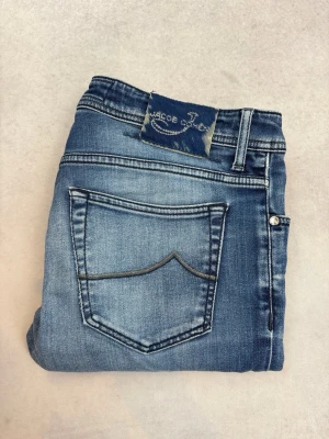 Blå slim fit jeans från Jacob Cohen - Snygga blå slim fit jeans från Jacob Cohen med klassisk femficksdesign och slitna detaljer. Jeansen har en ljus tvätt med subtila whiskers och kontrastsömmar. Perfekta för en avslappnad och trendig look.