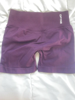 Lila Impact shorts  DFYNE - Snygga lila seamless shorts från DFYNE med hög midja och tight passform. Perfekta för träning eller chill. Mjukt och stretchigt material som sitter skönt på kroppen. Logga framtill och baktill i vitt.