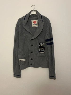 Cardigan - Hej nu säljer vi denna grymt feta 55 stage cardigan i en stilren grå färg som lätt gör att klä sig bra i. Skicket 9/10 inga defekter. Storleken: M. Bröstlängd: 45cm. Midjalängd: 45cm. Längd:60cm. Armlängd: 65cm. För fler frågor hör gärna av er så hörs vi!