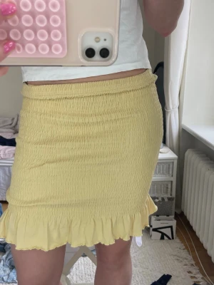 Smockad kjol - Söt kort gul kjol med smockad midja och volangkant nertill. Tillverkad i ett lätt och mjukt material som känns skönt mot huden. Tveka inte om frågor eller funderingar!💛⭐️