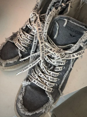 Gråa high top sneakers Zadig & Voltaire - Unika gråa high top sneakers från Zadig & Voltaire med slitna, fransiga kanter och vita snören med logotyp. Dom har en cool look som sticker ut. 