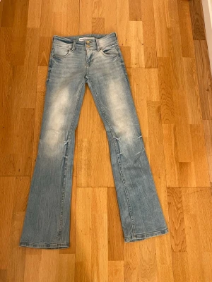 Ljusblå bootcut jeans med slitningar - Säljer ett par ljusblå bootcut jeans med snygga slitningar och tvättade detaljer på benen. Jeansen har klassisk femficksmodell, normal midja och utsvängda ben. 