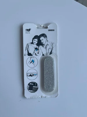 Glittrig mobilhållare Ale-Hop - Snygg och praktisk mobilhållare från Ale-Hop i silverfärgat glitter. Perfekt att fästa på baksidan av mobilen för bättre grepp eller använda som stöd.