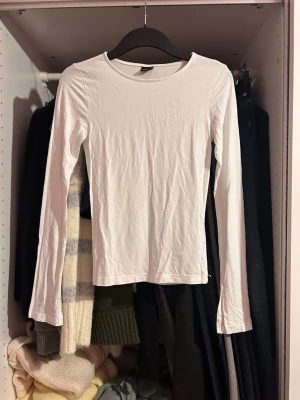 Vit långärmad topp från Gina Tricot - En basic vit långärmad topp från Gina Tricot i mjuk bomull. Modellen har rund halsringning och en slim passform som sitter snyggt på kroppen. Perfekt att styla med jeans eller kjol för en clean look.