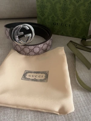 GG Supreme bälte med silverdetalj - Säljer ett exklusivt GG Supreme bälte från med klassiskt monogrammönster i beige och brunt. Bältet har en stor, rund silverfärgad GG-logo som spänne och är tillverkat i canvas med skinn på insidan. Perfekt för att lyfta din outfit.