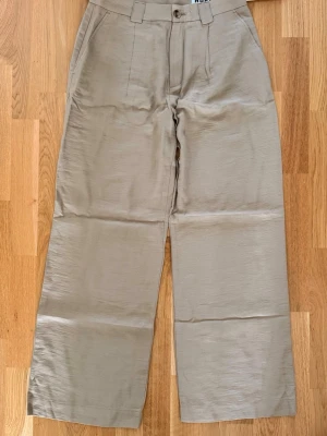 HOPE unisex byxor 36/44 beige - helt ny! - Stilrena beiga chinos från Hope med rak och vid passform. Byxorna har klassiska fickor fram, en bakficka med knapp och hällor för bälte. Tillverkade i ett lätt, slätt tyg som ger en snygg och modern