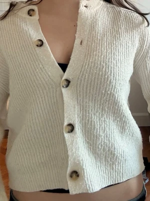vit kofta från Zara med knappar - Snygg krämvit kofta från Zara med marmorerade knappar framtill. Koftan har rund halsringning, ribbstickad struktur och långa ärmar. Perfekt att slänga över en topp för en chill look. Skriv för mer bilder. 