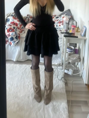 Svart volangkjol - Supersnygg svart kortkjol med volanger i mjuk sammet. Kjolen har en elastisk midja och bra passform, passar perfekt till både boots och sneakers. Enkel att styla för både fest och vardag. Tycker den ser stor ut på mig, är 167 och åt det tunnare hållet.