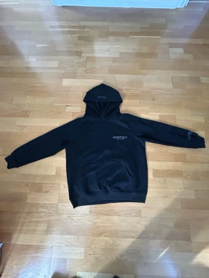 Svart Essentials Fear of God hoodie - Svart hoodie från Essentials Fear of God med klassisk huva och känguruficka. Diskret logga på bröstet och patch på huvan. Oversized passform och mjukt material som känns riktigt skönt. Perfekt för en avslappnad streetwear-look. Passar perfekt på medium men om man gillar mer över size funkar det också perfekt för s. Priset är förhandlingsbart.