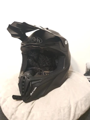 Airoh crosshjälm svart i storlek L - Svart crosshjälm från Airoh med skärm och ventilationsöppningar. Snygga ljusa detaljer på sidorna och vadderad insida för bra passform. Synliga tecken på slitage på utsidan men inget som påverkar skyddet. Storlek L 59-60. Nypris för liknande hjälmar omkring 3800-8000.  Vill få 1200 eller kom med bud.