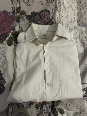 Vit skjorta från Tiger of Sweden - Säljer en klassisk vit skjorta från Tiger of Sweden i slim fit. Skjortan har knappar framtill och en snygg krage. Perfekt för dig som gillar stilrena plagg och vill ha något som funkar till många olika looks.