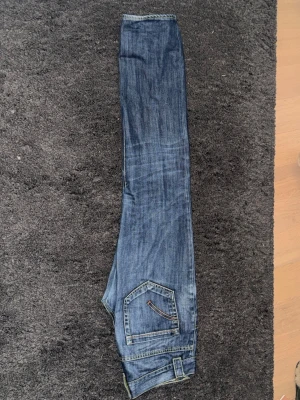 Dondup stan art - Säljer ett par klassiska blå jeans med raka ben och snygga kontrastsömmar. Jeansen har fem fickor och coola detaljer på bakfickan. Perfekta till en avslappnad stil och tillverkade i slitstarkt denimtyg.
