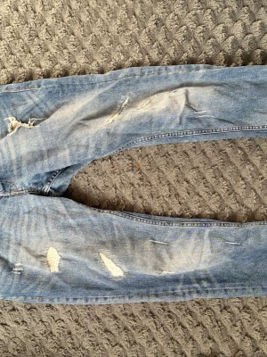 Ljusblå slitna jeans Jack & Jones - Säljer ett par ljusblå jeans från Jack & Jones med flera slitningar och hål på benen. Jeansen har klassisk femficksmodell och smal passform. Perfekta för en avslappnad och trendig stil.