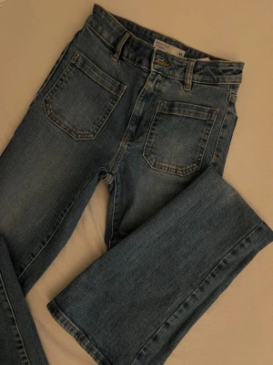 Blå bootcut jeans från Cubus - Säljer ett par klassiska blå bootcut jeans från Cubus i storlek XS, eftersom dom tyvärr inte passar mig. Jeansen har hög midja, raka ben och fickor både fram och bak. Tillverkade i slitstark denim med snygga sömmar och bälteshällor. Perfekta för en avslappnad och trendig look. Samt passar väldigt bra för våra snygga långa tjejer💞