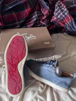 Blåa Christian Louboutin sneakers - ÄKTA OCH KVITTO KOMMER MED!!! Snygga blåa sneakers från Christian Louboutin med klassisk röd sula och vita kanter. Skorna har lågt skaft, blå mocka på ovandelen och matchande blå skosnören. Perfekta för dig som vill sticka ut med exklusiva detaljer och ikonisk design. KVITTO FINNS!!!