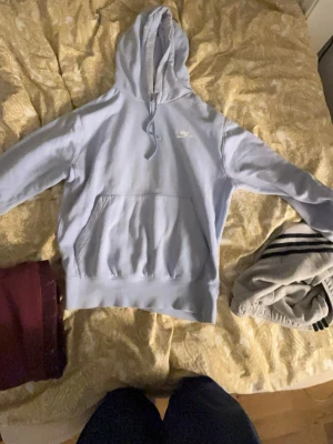 Ljusblå hoodie från Nike - Säljer en ljusblå hoodie från Nike med klassisk logga på bröstet. Hoodien har en stor känguruficka framtill, justerbar huva med dragsko och ribbade muddar vid ärmar och nederkant. Perfekt för en avslappnad och sportig stil.