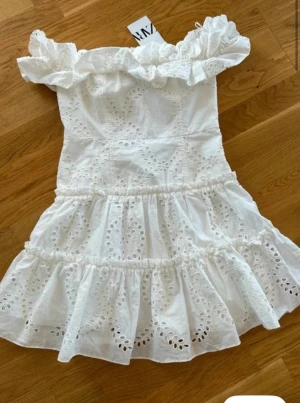 Vit offshoulder klänning från Zara - Superfin vit kortklänning från Zara med offshoulder och volangdetaljer. Klänningen har broderade hålmönster och är tillverkad i bomull. Perfekt för sommarens alla tillfällen och ger en romantisk vibe. Storlek S ny med prislapp 