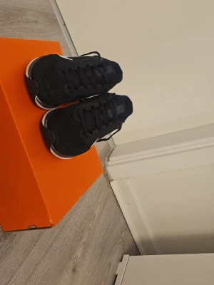 Svarta Nike sneakers med vit sula - Snygga svarta Nike sneakers med vit sula och klassisk vit swoosh på sidan. Ovandelen är i meshmaterial för bra andningsförmåga och komfort. Skorna har svarta skosnören och en sportig, stilren look som passar perfekt till streetwear.