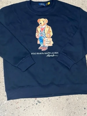 Mörkblå sweatshirt Polo Bear Ralph Lauren - Mörkblå sweatshirt från Ralph Lauren med ikoniska Polo Bear-trycket framtill. Rund halsringning, ribbade muddar och avslappnad passform. Perfekt för en chill och stilren look. Den är tvättad en gång alltså knappt använd. Säljer den då jag inte gillar den så mycket längre. Den är M men passar S