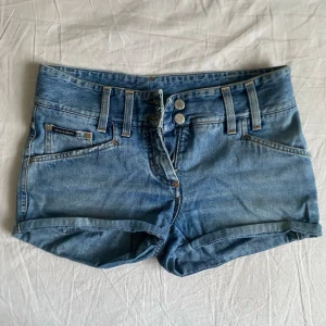 Lågmidjade jeansshorts från Dolce&Gabbana - Snygga lågmidjade blå jeansshorts från Dolce & Gabbana med dubbla silverknappar och dragkedja. Perfekta för en avslappnad stil under varma dagar. Vintagestil. Passar strl XS och S.