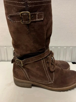 Höga stövlar brun mocka  - I storlek 40, knytning och spännedetalj, skadad vid skaftet annars i bra skick!