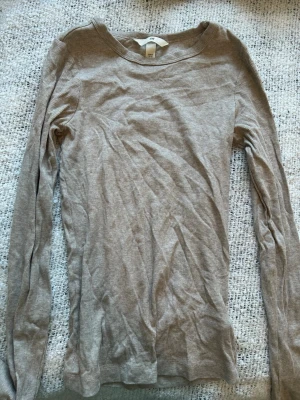 Beige ribbad långärmad topp H&M - En enkel och stilren beige långärmad topp från H&M i ribbad bomull. Perfekt basplagg med rund halsringning och smal passform. Passar till allt och är superenkel att styla med olika outfits.