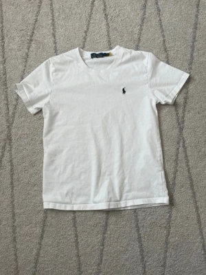 Vit t-shirt från Polo Ralph Lauren - Klassisk vit t-shirt från Polo Ralph Lauren med liten broderad logga på bröstet. T-shirten har rund halsringning och korta ärmar. Tillverkad i mjuk bomull för en skön och avslappnad stil.