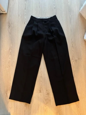 Svarta kostymbyxor från NA-KD - Bredare kostymbyxor från NAKD. Aldrig använda då det var lite för stora. Storlek 32 men stora i storleken och långa ben. Originalpris: 599kr 