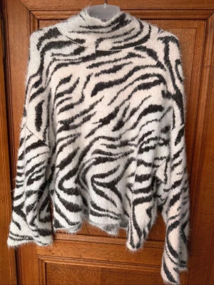 Zebramönstrad fluffig polotröja - Säljer en supermjuk stickad polotröja med zebramönster i svart och vitt. Tröjan har en hög krage, lång ärm och oversized passform. Perfekt för dig som vill sticka ut med en trendig och mysig look. Storlek xs men passar s också❤️